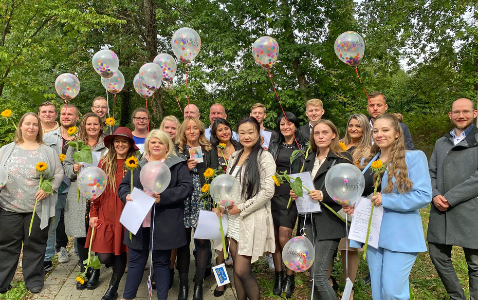 Gruppenfoto mit Luftballons und Blumen von 21 Altenpfleger und –pflegerinnen